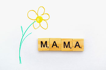 Grußkarte mit einer gemalten Blume und dem Wort "MAMA" welches aus einzelnen Buchstaben aus einem Brett-/Wortspiel zusammengesetzt sind.
